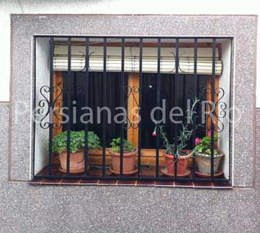 Alicantina de plástico blanca recogida sobre una ventana con reja y macetas