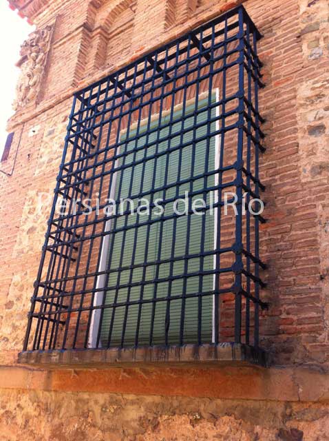 Alicantina de plástico verde dentro de la reja de un balcón en fachada de ladrillo
