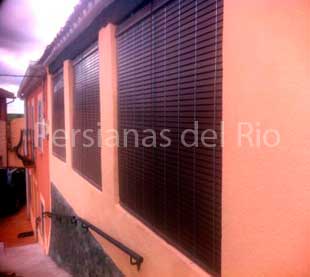 Persianas alicantinas de madera oscuras en las ventanas de una fachada naranja