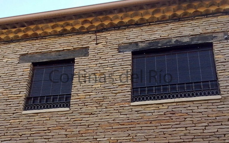 Dos ventanas de piedra con alicantinas de madera marrón oscuro