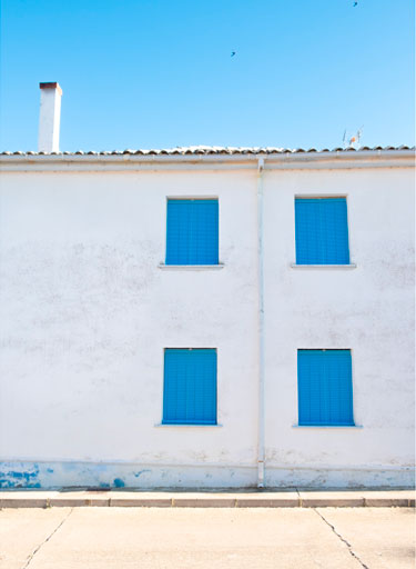 Cuatro alicantinas de plástico azules en las ventanas de una fachada blanca