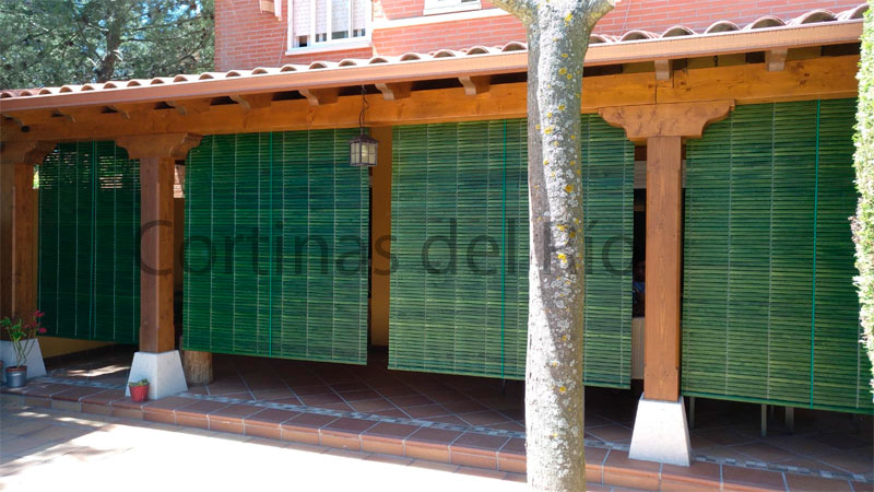 Persianas alicantinas de madera verdes entre los pilares de un porche