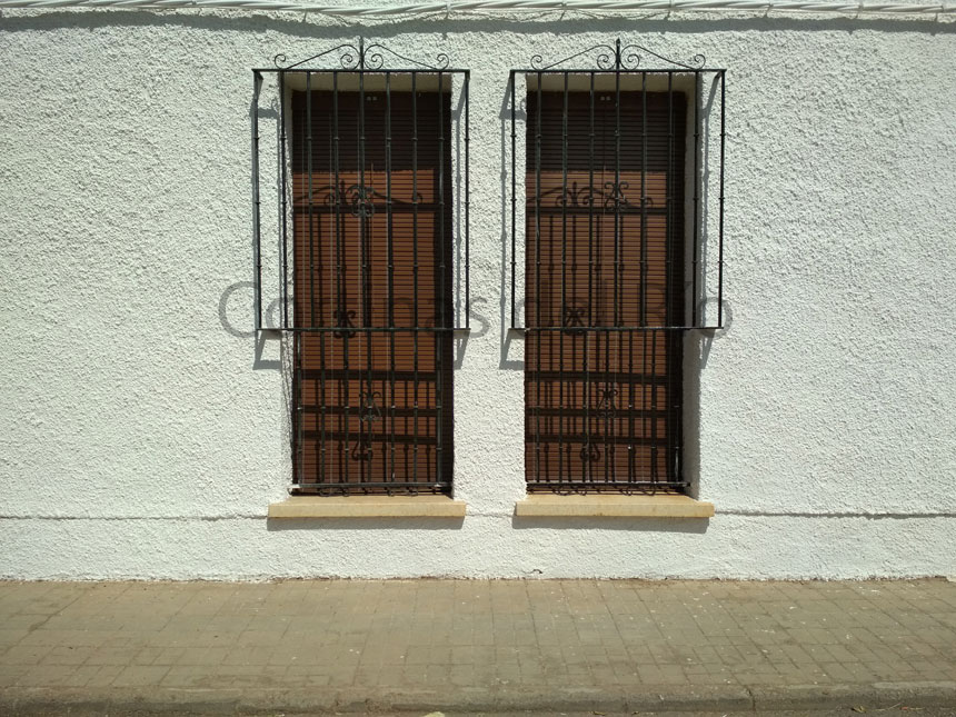 Persianas alicantinas de plástico marrones en dos ventanas estrechas con rejas